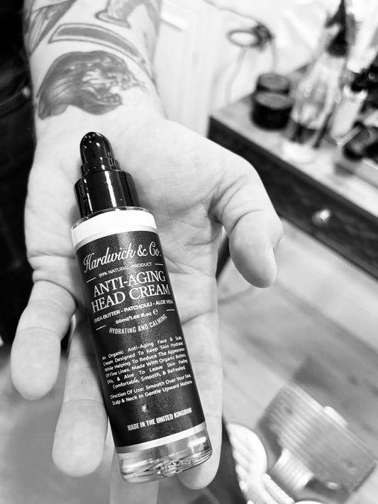 Hand holding a bottle of Hardwick & Co. anti-aging head cream with a blurred background.