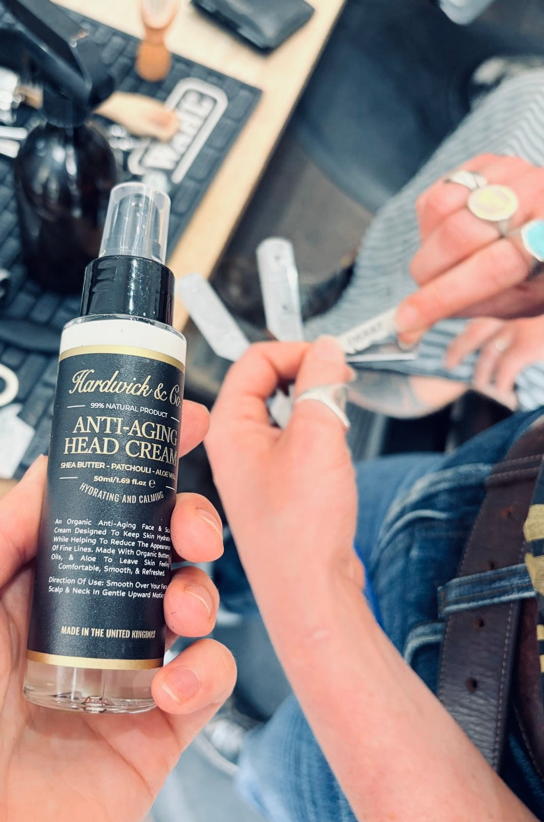 Hand holding a bottle of Hardwick & Co. anti-aging head cream with a blurred background.