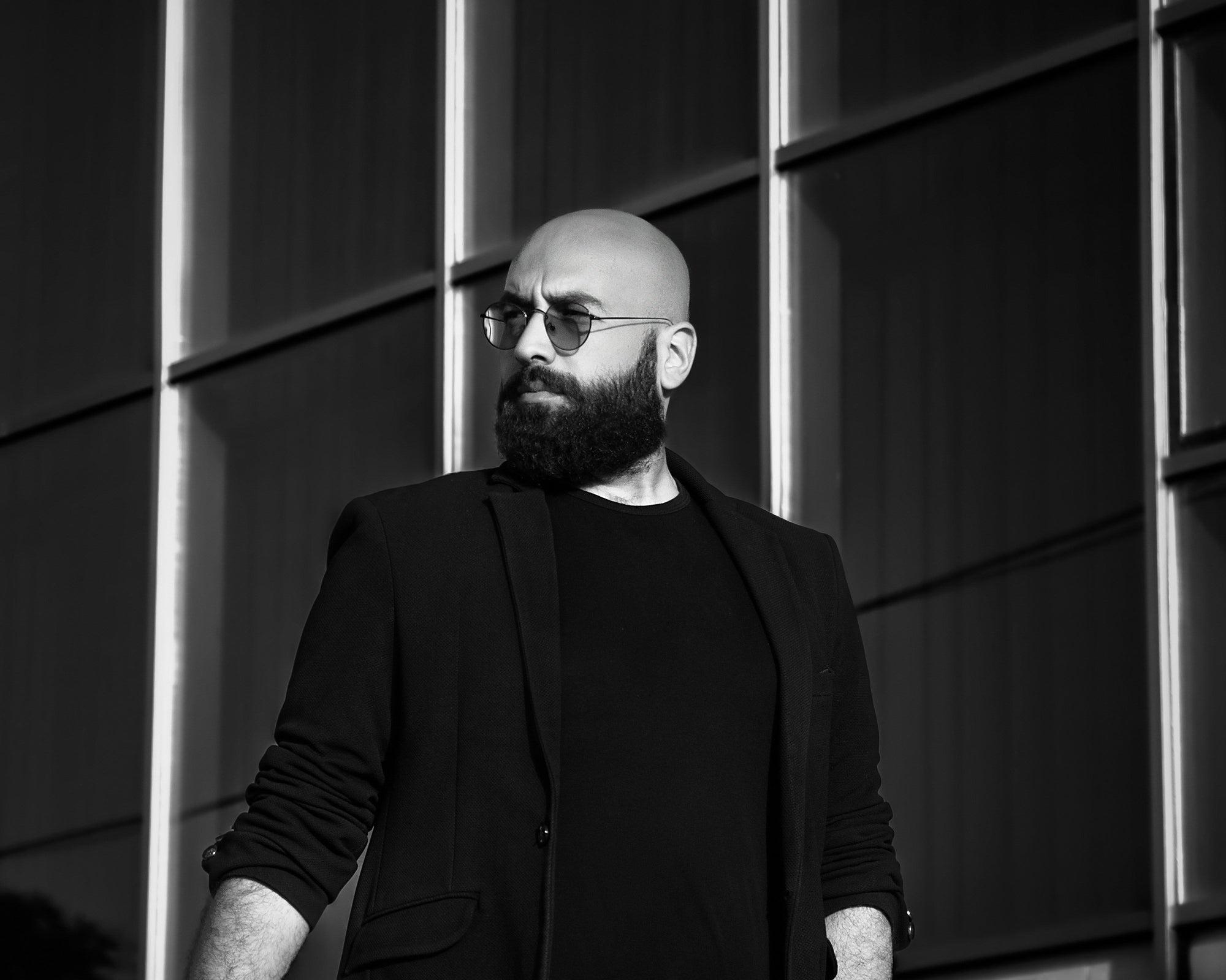 Man with a beard and sunglasses standing against a modern building facade