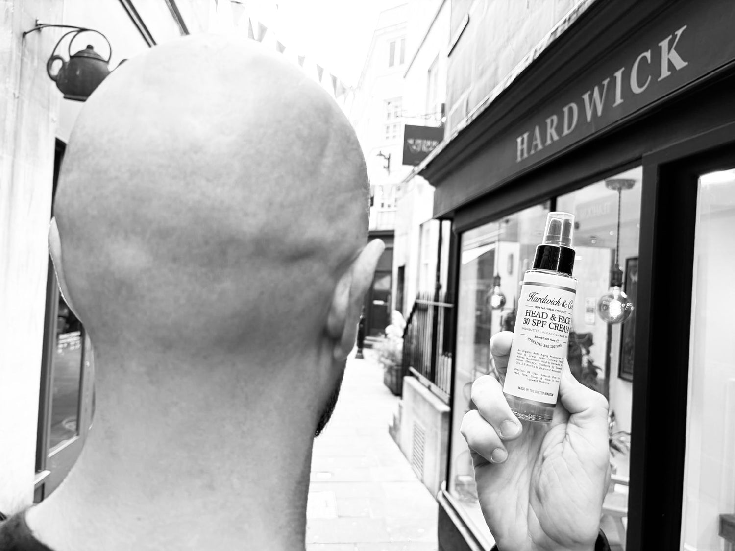 Person holding a bottle of Hardwick product in front of a store window.