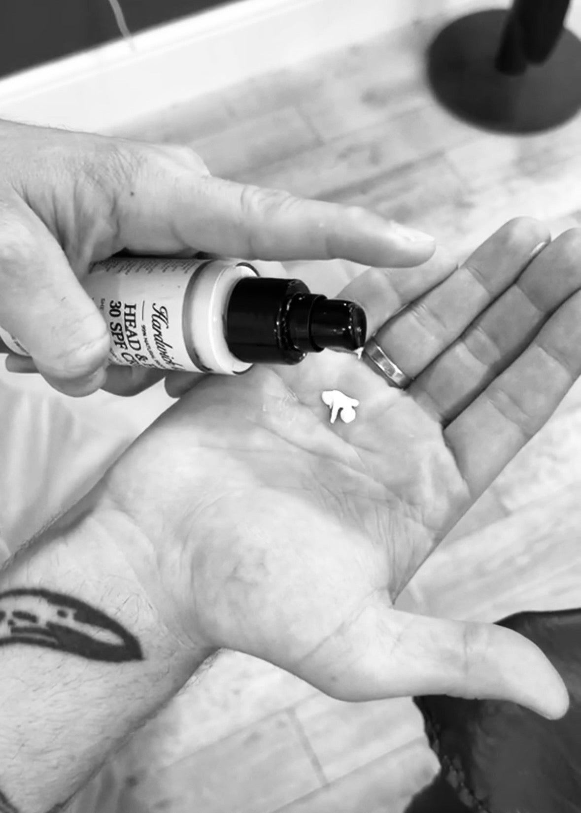 Person applying a small bottle of oil to their palm with a tattoo on their wrist.